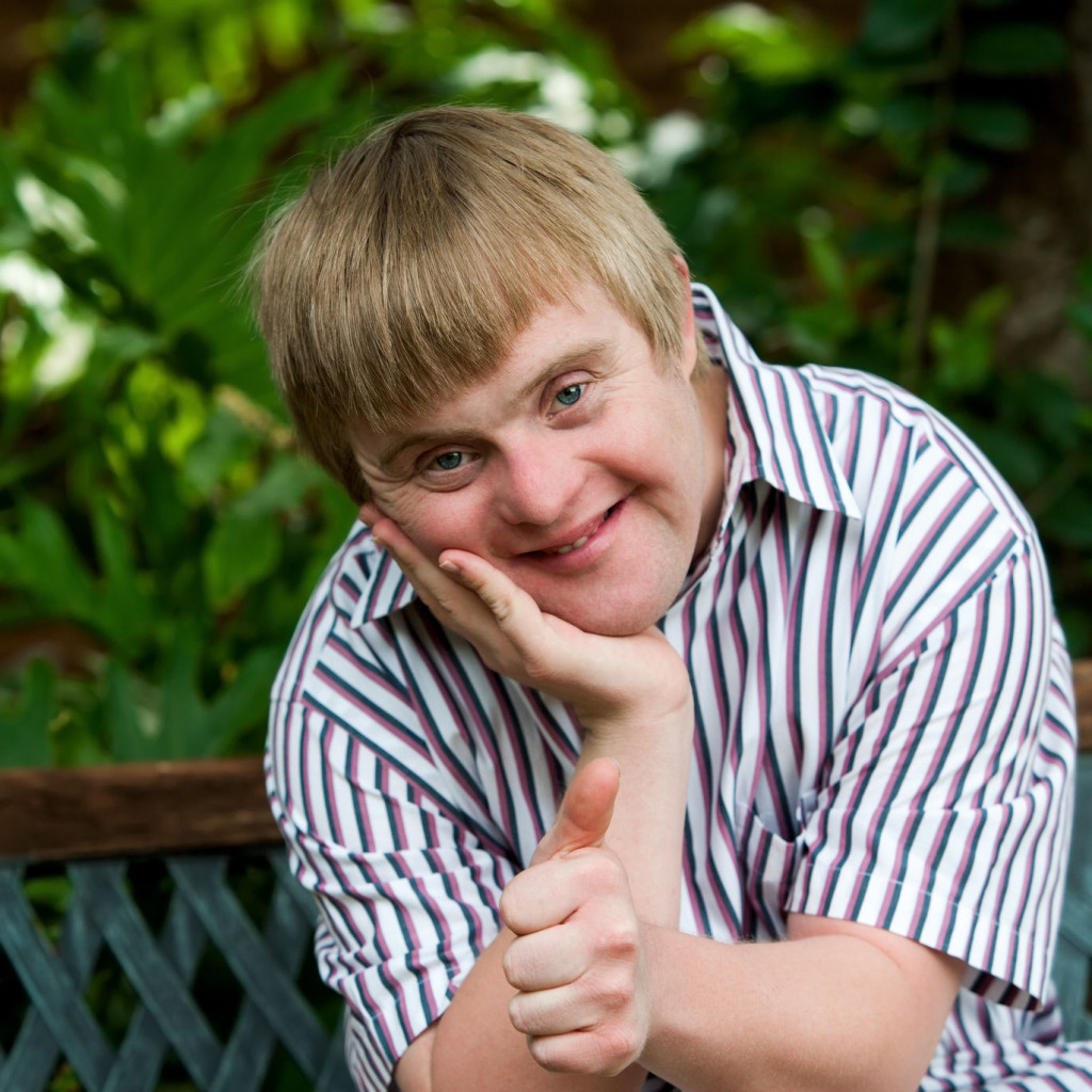 35501022 - close up portrait of cute boy with down syndrome doing thumbs up in garden.